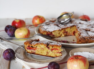 Laid table with a sweet round pie with apples and plums. Homemade biscuit charlotte with powdered sugar.