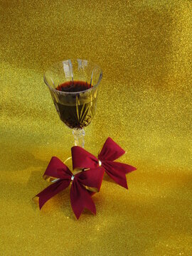Copa de cristal con vino tinto sobre fondo dorado diamantado y dos mo&ntilde;os aterciopelados en color guindo 4