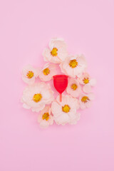 Pink menstrual cup with flowers on light pink background. Feminine hygiene background. Sustainable female care products.