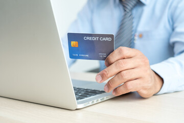 The businessman's hand is holding a credit card and using a laptop for online shopping and internet payment in the office