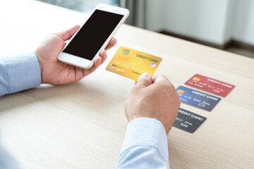 The businessman's hand is holding a credit card and using a smartphone for online shopping and internet payment in the office