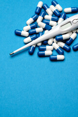 group of pills or capsules and electronic digital thermometer on blue background