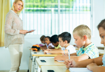 Fototapeta premium Portrait of focused tween boy writing exercises in workbook in classroom during lesson in elementary school