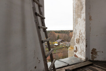 window in the church belfry with wooden stairs and view on village autumn landscape in cloudy day