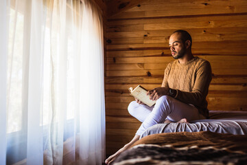 hombre pelón con barba leyendo un libro con un suéter para el frio - obrazy, fototapety, plakaty