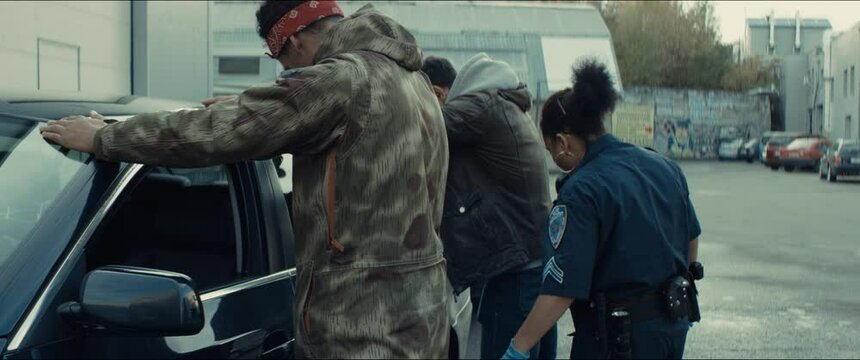 Police officer searches a suspect near a police vehicle in the street. Lights flashing in the background