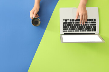 Female hands with modern laptop and cup of coffee on color background