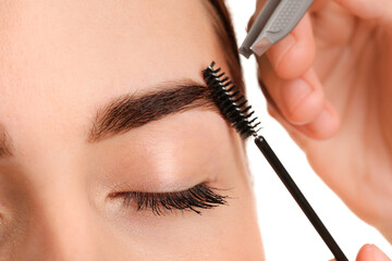 Young woman undergoing eyebrow correction procedure on white background, closeup