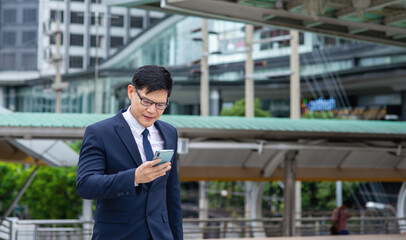 Confidence Asian businessman office worker walking on office district in the city using smartphone with internet for outdoor working. Wireless technology network and cooperate business concept.