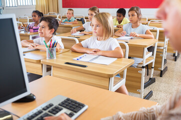 Fototapeta premium View from teacher of primary school pupils raising their hands in classroom