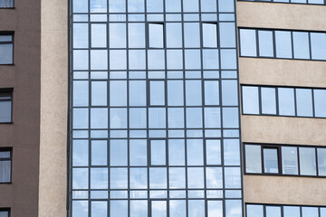 new multi-storey building of burgundy white color against the sky in the windows of which the sun is reflected