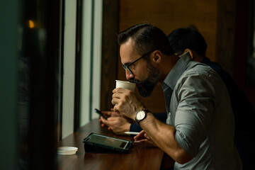 Caucasian man creative freelance sitting in coffee shop and drinking hot coffee with using digital tablet and pen for working. Businessman entrepreneur working with wireless technology in cafe.