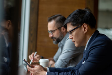 Asian businessman office worker sitting in coffee shop using smartphone with internet for online cooperate working or texting message. Business man entrepreneur working with wireless technology.