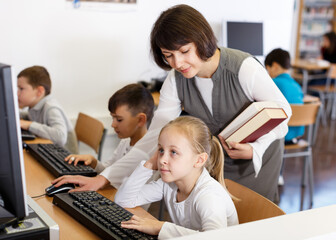 Obraz premium Friendly woman teacher helping tween girl during lesson in computer room of school library ..