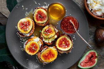 Sandwiches with figs on toasted baguette with goat cheese on a plate with honey, sesame seeds and walnuts. Fresh toast with figs and garnished with thyme leaves. Top view