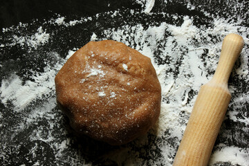 Dough, rolling pin and flour on a black background. Ginger cookie dough on a floured black surface. View from above. The dough has a brown tint. The concept of Cooking. Copy space for text