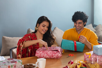 Young couple wrapping up presents for Diwali while being very happy about it	