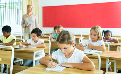 Portrait of focused tween schoolgirl writing exercises in workbook in classroom during lesson