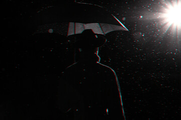 dark silhouette of a man in a raincoat and hat under an umbrella on the street in the rain