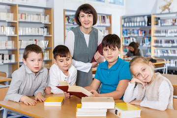 Group of school kids studying in school library with friendly female teacher..