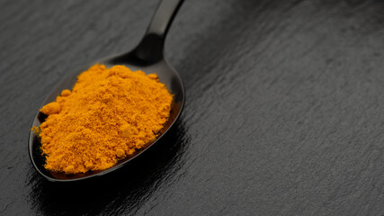 turmeric powder in spoon on black stone, top view. Condiment or dietary supplement