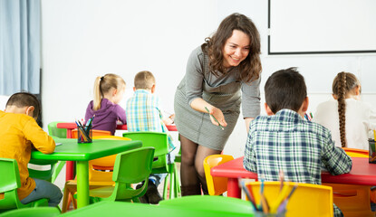 Friendly teacher woman helping children during lesson in schoolroom..