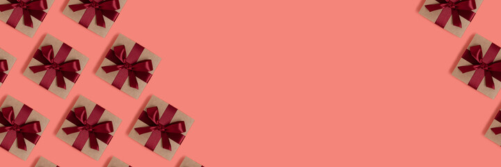 Pattern made of gift boxes tied with red ribbons on a coral background with copy space. Holidays concept banner.