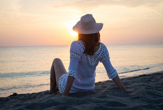 Young Woman In White Dress And Hat Sitting On Sandy Beach In Sunset Looking To Horizon Woman In Vacations In Sunset On Ada Bojana Beach In Montenegro