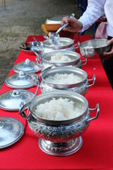Scoop rice into a Thai patterned aluminum bowl for offering to monks on religious days.