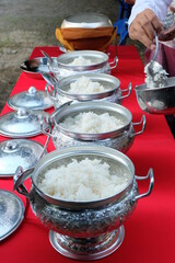 Scoop rice into a Thai patterned aluminum bowl for offering to monks on religious days.