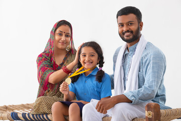 PORTRAIT OF A SMALL RURAL GIRL HAPPILY POSING WITH GOLD MEDAL ALONG WITH PARENTS
