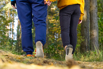 Mom with daughter walking in nature on the forest road holding hands. Mother with daughter hiking in autumn pine forest.