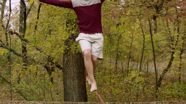 Caucasian man practicing slackline in the autumn forest. A man practices highlining in the autumn forest at dawn.