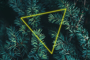 Creative yellow triangle fluorescent neon frame in Christmas tree branches with copy space for cold...