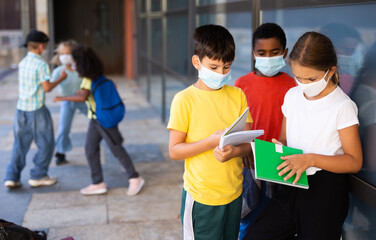 Fototapeta premium Portrait of three primary school children wearing face masks talking outside before lesson