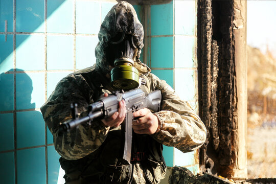 military man in a gas mask, hooded, aiming to point his weapon at the camera