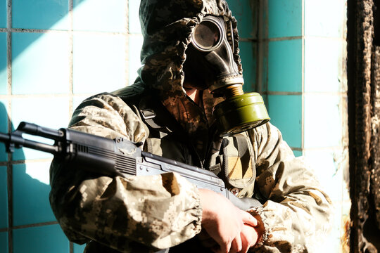 military man in a gas mask, hooded, holding a weapon in his hands, stands at the window of the destroyed building
