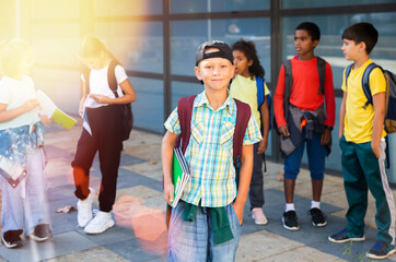 Smiling boy standing after classes near school with fellow classmates on background