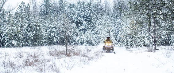 Fotobehang Athlete rides a snowmobile in the mountains. Snowmobile in snow. Concept winter sports. A man is riding snowmobile in mountains. Pilot on a sports snowmobile in a mountain forest © Yevhen