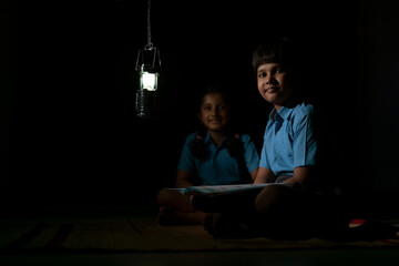 PORTRAIT OF A RURAL BOY AND GIRL STUDYING AT NIGHT AND SMILING AT CAMERA
