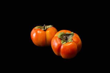 Two persimmons on black background. Orange fruit on dark surface.