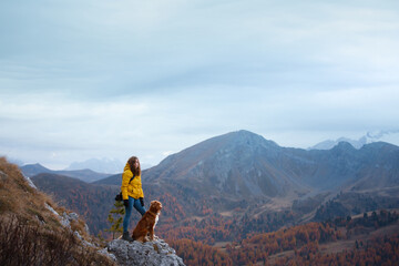girl with a dog in the mountains. travel, Nova Scotia Duck Tolling Retriever with with a woman in a yellow jacket stand on a stone near a cliff