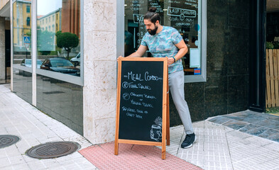 Young waiter placing a blackboard with the daily menu in front of the restaurant facade © David Pereiras