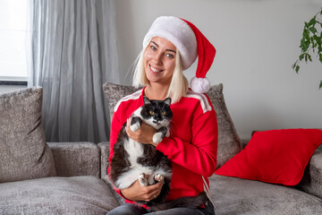 Woman in Christmas red hat sitting on the sofa with cat.