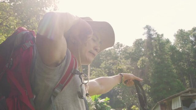 Slow motion of Tired young Asian man backpacker hiking in beautiful forest mountain to the camp. Healthy handsome guy relax and enjoy outdoor lifestyle in summer holiday vacation