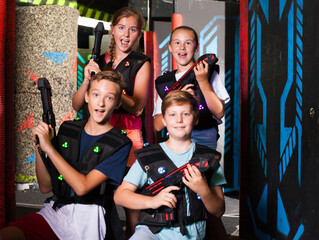 Cheerful teen girls and boys with laser pistols posing together in dark laser tag labyrinth..