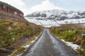 Snow flakes falling on a small asphalt road which leads into mountains covered with snow. Nobody. Gleniff Horseshoe Drive, county Sligo, Ireland