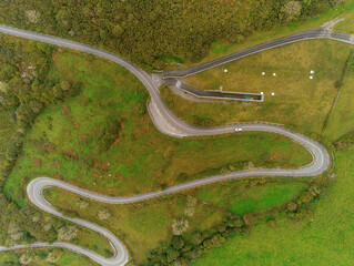 Winding narrow road on a hill in Burren, Ireland. Aerial drone view. Green fields and small trees around the pass.