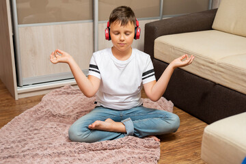 Boy in headphones listening to music. He is lying near the sofa. He is meditating and enjoying.