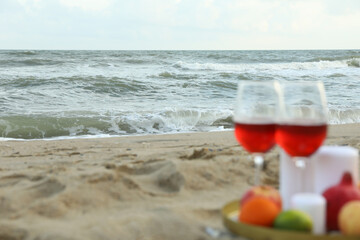 Tray with glasses of wine, fruits and candles on sandy sea beach